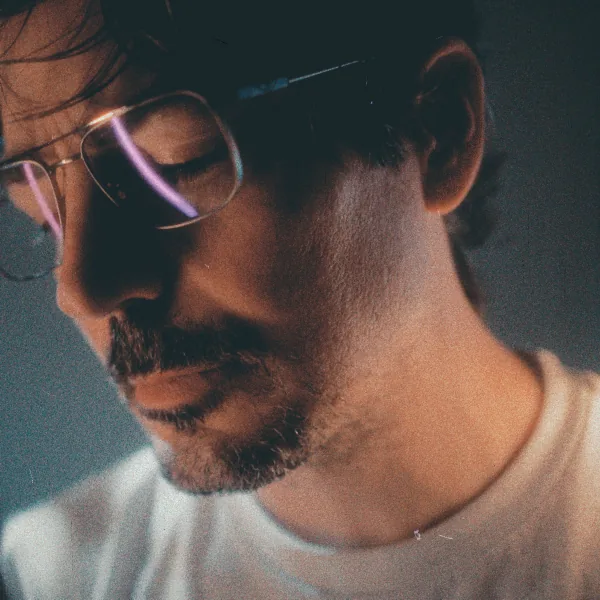 Cover art for STATIC: a close-up of Lluís looking down, his glasses catching a purple light