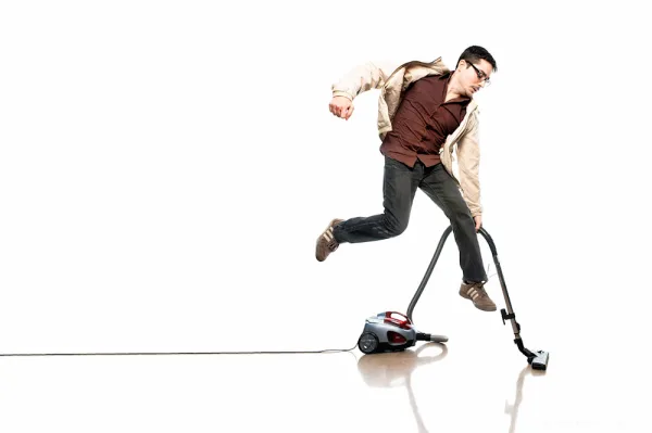 Man jumping while using a vacuum cleaner, on a white seamless background